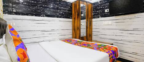 A hotel room with a bed, a wooden wardrobe, a mirror, and a TV.