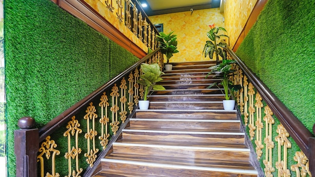 Una escalera con escalones de madera y barandillas doradas ornamentales, flanqueada por muros de césped artificial verde.