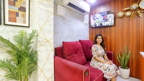 Un sofá rojo en una habitación con una pared de mármol, un televisor montado y una planta en maceta.