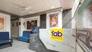 Ein Hotel-Empfangsbereich mit Marmor-Rezeptionstresen, blauer Sitzgelegenheit, gerahmten Kunstwerken und einem Deckenventilator.