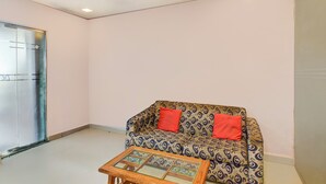 A living room with a patterned sofa, a glass coffee table, and a door with a glass panel. - Fabhotel Devi Residency Wakad (Paud)