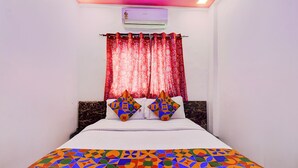A neatly made bed with a colorful geometric-patterned bedspread, a white wall, and a red curtain. - Fabhotel Devi Residency Wakad (Paud)