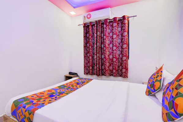 A hotel room with a bed, a nightstand, a telephone, and a window with red curtains. - Fabhotel Devi Residency Wakad (Paud)