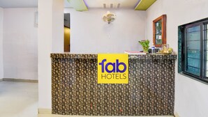 A hotel reception area with a modern design, featuring a textured reception desk, a ceiling light fixture, and a window with a view. - Fabhotel Devi Residency Wakad (Paud)