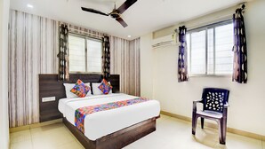 A bedroom with a bed, a ceiling fan, a window with curtains, and a chair. - Fabhotel Galaxy Inn I (Pune)