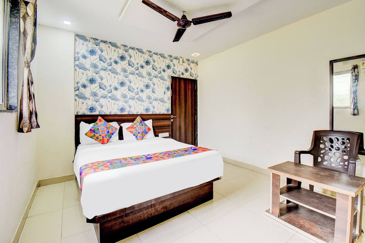 A bedroom with a wooden bed, colorful pillows, a small wooden table, and a ceiling fan.