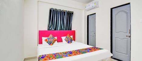Una cama con colcha de estampado geométrico y llamativos colores, cabecera rosa y dos almohadas decorativas.
