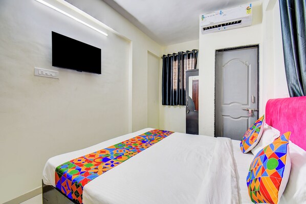 Une chambre d’hôtel avec un lit, un téléviseur à écran plat fixé au mur, une porte avec un rideau et une fenêtre également dotée de rideaux.