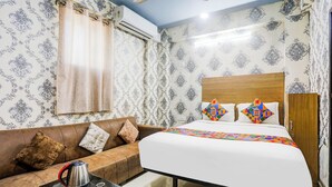 A bedroom with a bed, a sofa, a coffee table, and an air conditioning unit. - Fabhotel Dream Inn (Danapur)