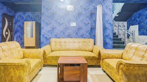 A living room with a yellow sofa set, a wooden coffee table, and a blue patterned wall. - Fabhotel Dream Inn (Danapur)