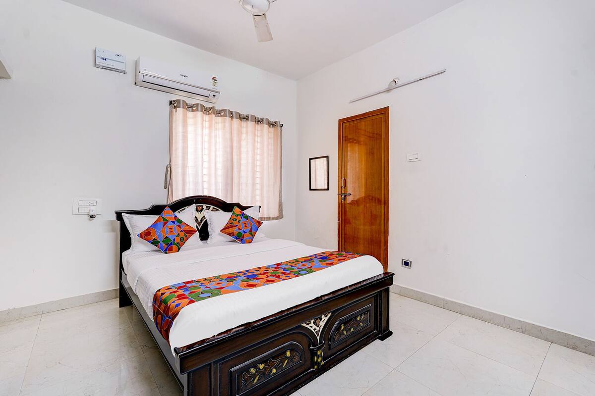 Quarto com cama, ar condicionado, porta de madeira e interruptor na parede.