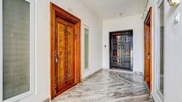 A hallway with marble flooring, wooden doors, and a black metal gate. - Fabhotel Ak Elite Luxury Homestay (Tirupati)