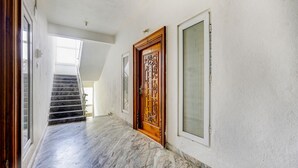 A hallway with a marble floor, a wooden door with intricate designs, and a window with frosted glass. - Fabhotel Ak Elite Luxury Homestay (Tirupati)