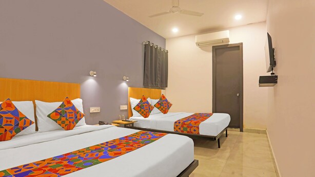 A hotel room with two beds, each with patterned bedspreads and pillows, a ceiling fan, an air conditioning unit, a TV mounted on the wall, and a bedside table with a lamp. - Fabhotel Vivek Inn (Prayagraj)