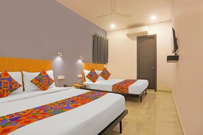 A hotel room with two beds, each with patterned bedspreads and pillows, a ceiling fan, an air conditioning unit, a TV mounted on the wall, and a bedside table with a lamp. - Fabhotel Vivek Inn (Prayagraj)