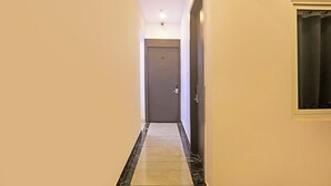A narrow hallway with a marble floor, a door at the end, and a window on the right. - Fabhotel Vivek Inn (Prayagraj)