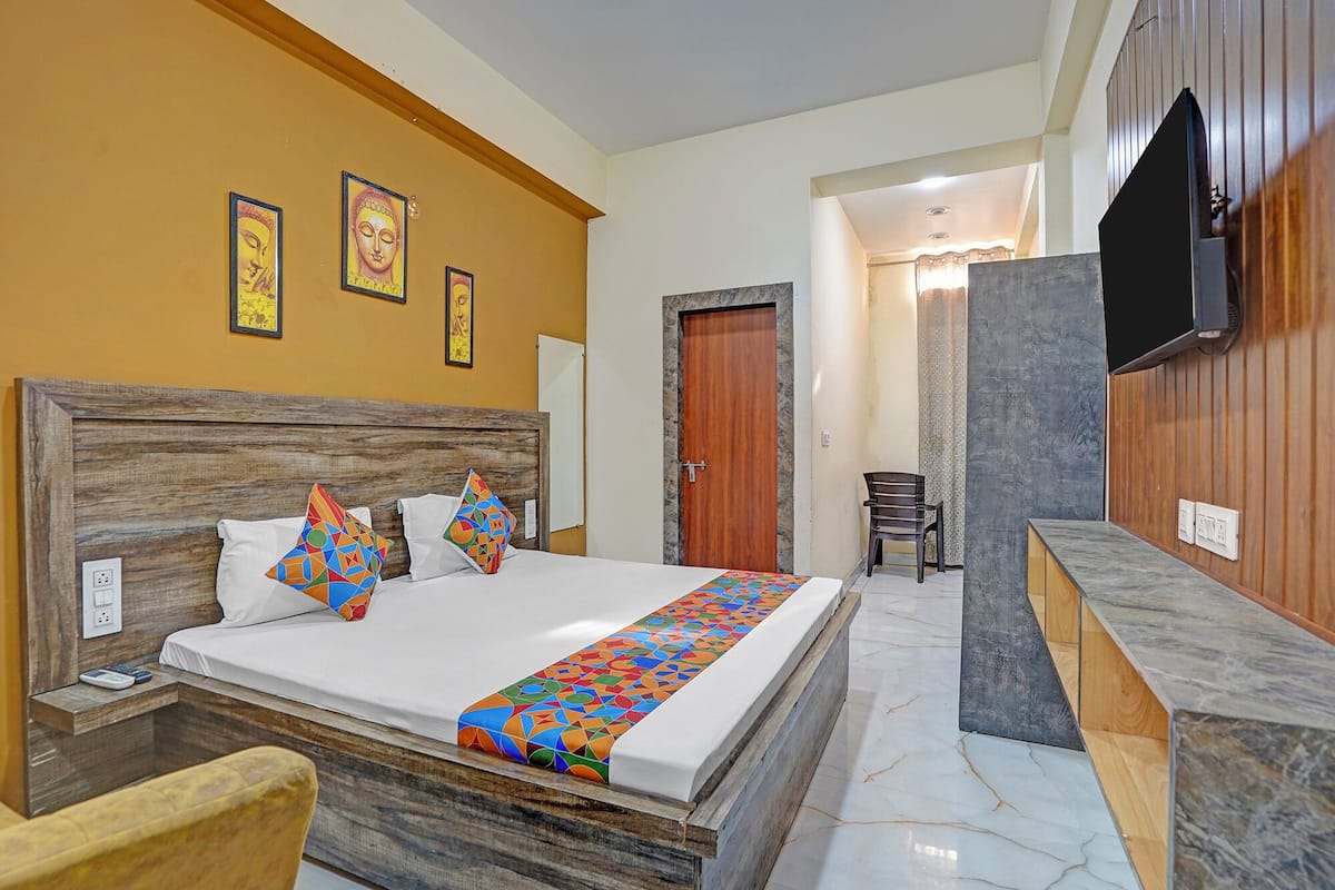 Ein Hotelzimmer mit Holz-Kopfteil, einem Bett mit farbenfroher, geometrischer Bettwäsche, einem an der Wand montierten Fernseher und einer kleinen Sitzecke mit einem Sessel.