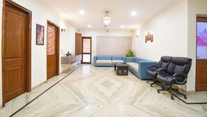 A spacious living room with a blue sofa, a black office chair, a coffee table, and a chandelier. - Fabhotel Tulip Residency (Gurugram)