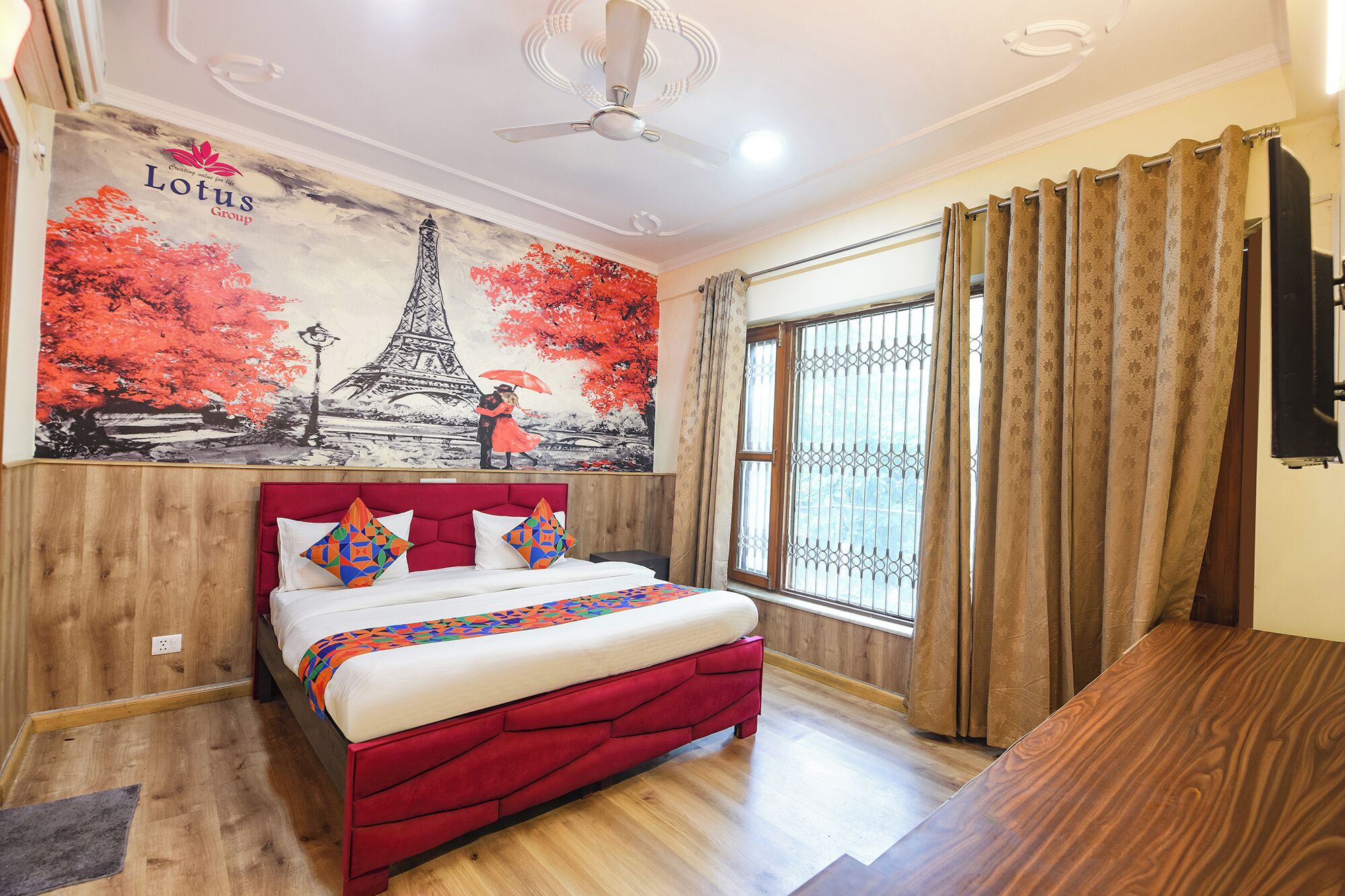 A hotel room with a bed, a ceiling fan, a window with curtains, and a mural of the Eiffel Tower.