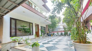 A courtyard with a checkered floor, potted plants, and a building with a balcony. - Fabhotel Tulip Residency (Gurugram)