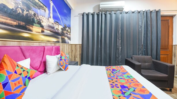 A hotel room with a bed, a chair, a curtain, and a wall with a mural. - Fabhotel Tulip Residency (Gurugram)
