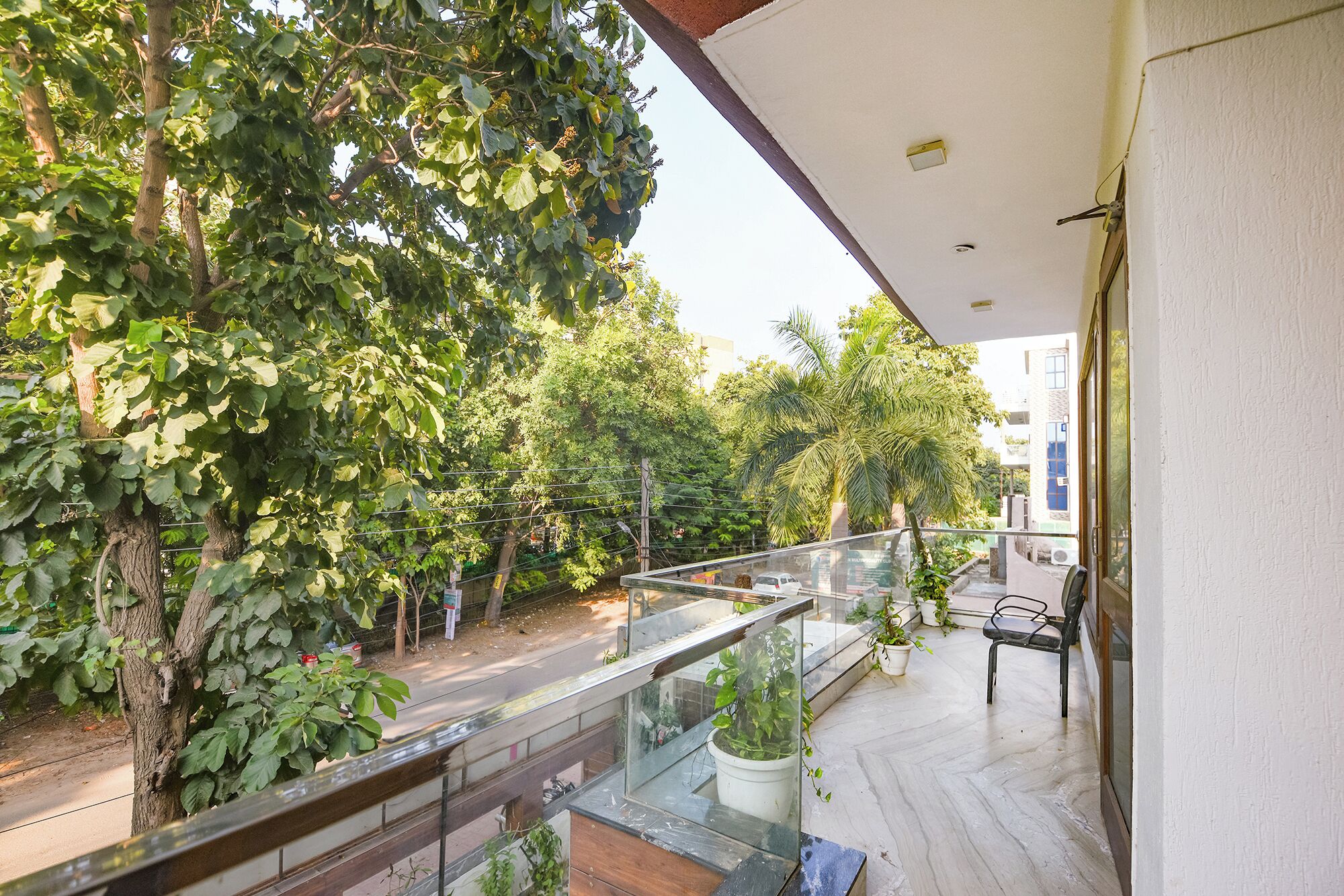 A balcony with a glass railing overlooking a street with trees and buildings.