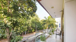 A balcony with a glass railing overlooking a street with trees and buildings. - Fabhotel Tulip Residency (Gurugram)