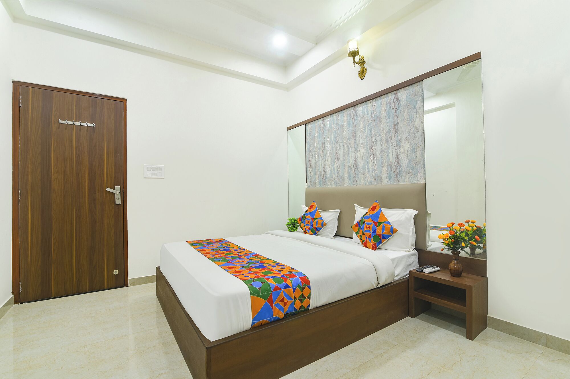 A bedroom with a bed, a nightstand, a mirror, and a door.