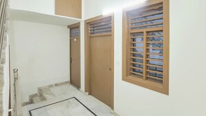 A hallway with a tiled floor, wooden doors, and a window with horizontal bars. - Fabhotel Lotus (Agra)