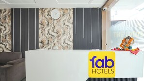 A reception desk with a 'fab hotels' sign, a clock, and a decorative statue with marigold flowers. - Fabhotel Lotus (Agra)