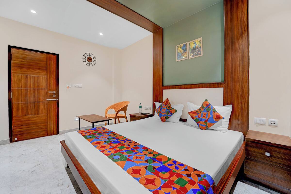 Ein Hotelzimmer mit einem Bett, einer Holztür, einem kleinen Tisch, einem Sessel und einer Wanduhr.
