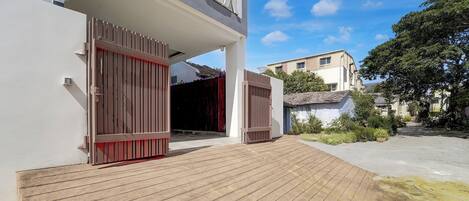 Un edificio moderno con una terraza de madera que conduce a una entrada protegida por una reja.