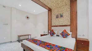 A bedroom with a large bed, a wooden headboard, a small bedside table, and a nightstand. - Fabhotel Kayal Plaza (Coimbatore)