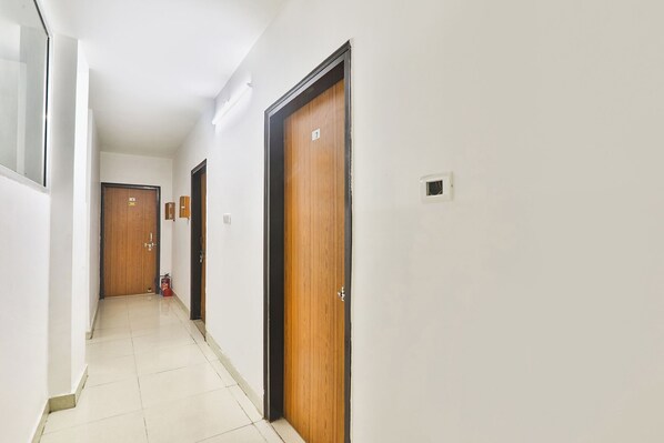 A hallway with wooden doors, white walls, and a tiled floor. - Fabhotel Raas Inn (Lucknow)