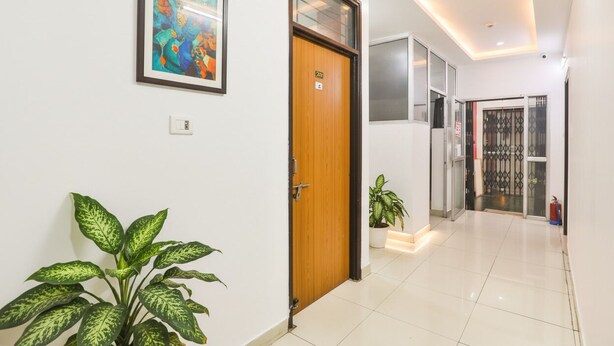 A hallway with a wooden door, a potted plant, and a framed artwork on the wall. - Fabhotel Raas Inn (Lucknow)