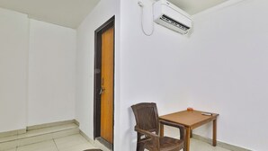 A small room with a wooden door, a single chair, a small table, and an air conditioning unit mounted on the wall. - Fabhotel Raas Inn (Lucknow)