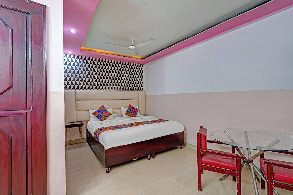 A bedroom with a bed, a ceiling fan, a patterned wall, a red chair, and a glass table.