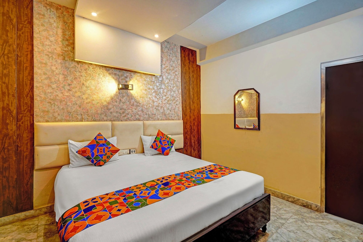 A hotel room with a large bed, a wooden headboard, a floral-patterned wall, and a mirror.