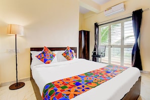 A hotel room with a bed, a standing lamp, a window with curtains, and an air conditioning unit. - Fabhotel Aura Suites (Pune)