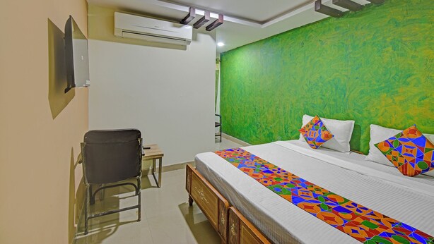 A bedroom with a green textured wall, a bed with a colorful geometric bedspread, a wooden nightstand, a chair, and an air conditioning unit. - Fabhotel Ayaansh Himayatnagar (Hyderabad)