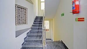 A stairwell with a fire extinguisher mounted on the wall, an exit sign, and barred windows. - Fabhotel Ayaansh Himayatnagar (Hyderabad)