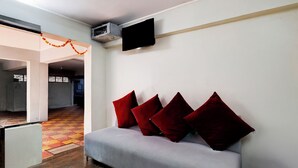 A modern living room with a grey sofa, red cushions, and a flat-screen TV mounted on the wall.