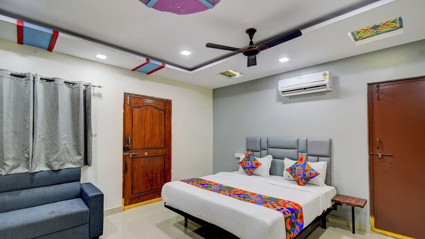 A bedroom with a bed, a blue sofa, a ceiling fan, and an air conditioning unit.