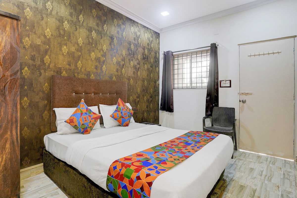 A bedroom with a bed, two pillows, a chair, a window with curtains, and a door.