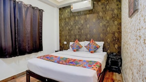 Une chambre d’hôtel avec un lit, une table de chevet, un appareil de climatisation et un papier peint à motifs.