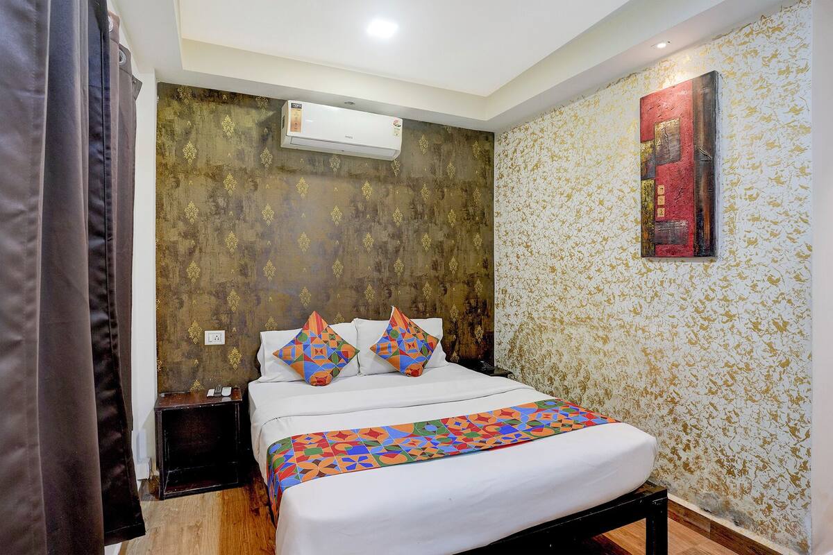 A hotel room with a bed, a nightstand, an air conditioning unit, and a wall with a textured pattern.