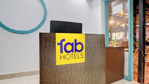 Un comptoir d’accueil orné d’une enseigne indiquant « fab hotels », un panneau en bois et une porte vitrée donnant sur un espace repas aménagé avec des meubles en osier.