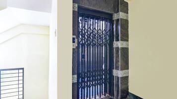 A black metal gate with a geometric pattern, set in a corner with a marble-like wall and a white door frame.