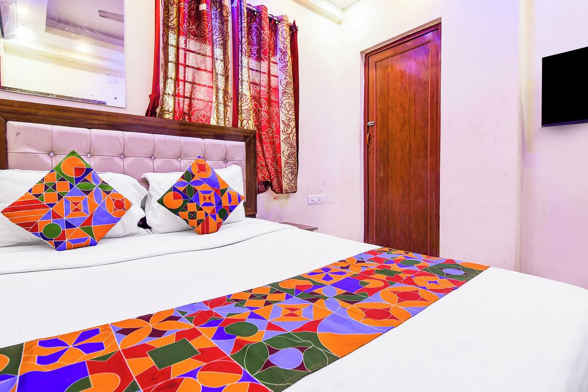 Un dormitorio con una cama, almohadas, una puerta de madera y un televisor en la pared.