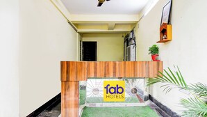 Ein Empfangsschalter mit einem Schild 'fab hotels', ein Deckenventilator, ein Topfpflanze und ein kleiner Gartenbereich.